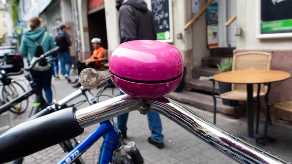 Dükkanlı pembe bisiklet zili ve arka planda yürüyen insanlar.