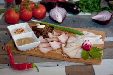 Tahta bir tahtanın üzerinde yaban turpu sosu ve ahşap bir masada hardal ile çeşitli pastırmalar.