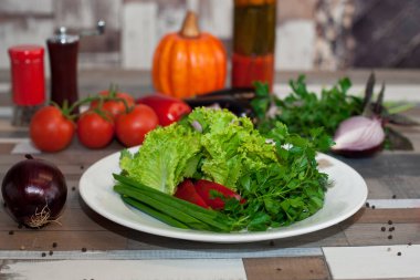 Tahta bir masada beyaz bir tabakta çeşitli taze dereotu, maydanoz, soğan ve biber. Vejetaryen yemeği.