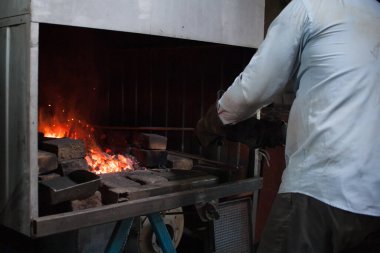 Bölünmüş bir ocakta demirci demircilik yapmak için metali ısıtır. Metal dövmesi işe yarıyor