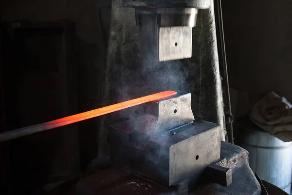 Blacksmithing. The blacksmith at the automatic hammer is forging split iron. Close-up photo of red metal