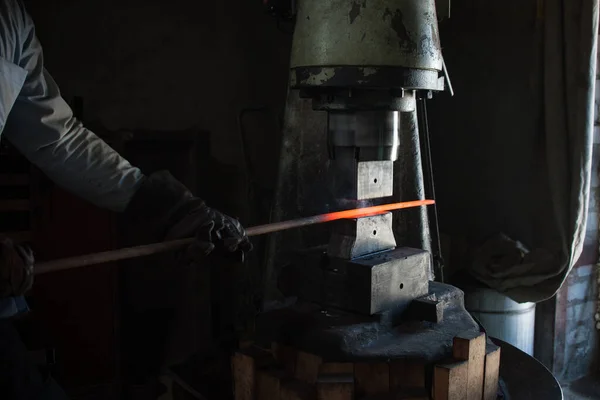 Blacksmithing. The blacksmith at the automatic hammer is forging split iron. Close-up photo of red metal