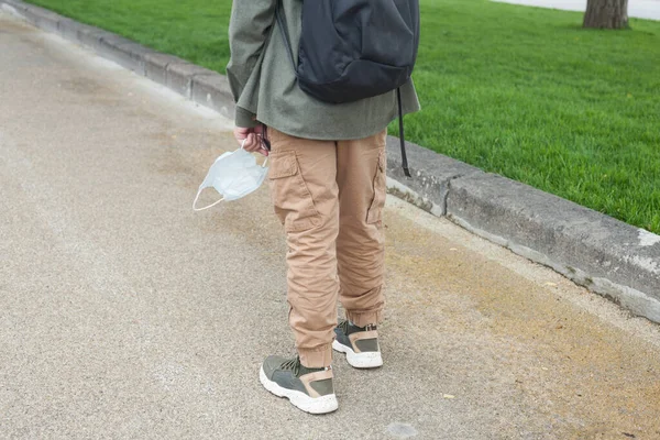 Beyaz tişörtlü ve elinde kitaplarla tıbbi maske olan Avrupalı bir çocuk okula gidiyor.