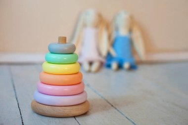 Ahşap oyuncak, çok renkli piramit çocuk odasının zemininde, arka planda iki tavşan var. Pastel renkli fotoğraflar
