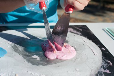 Şef bir rulo pembe dondurma yapıyor. Karışımı buz yüzeyine dağıtıyor..