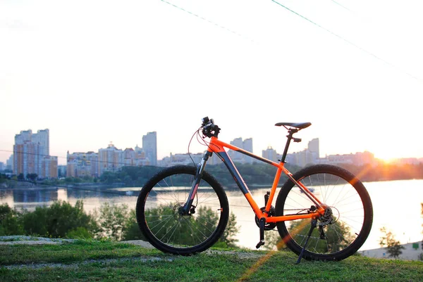 orange mountain bike near the river against the backdrop of the city and sunset