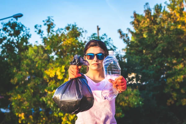 Young woman holding full trash bag and used plastic bottle in her hands. Plastic and food waste concept. Clean planet Earth, collect garbage, avoid pollution, save environment.