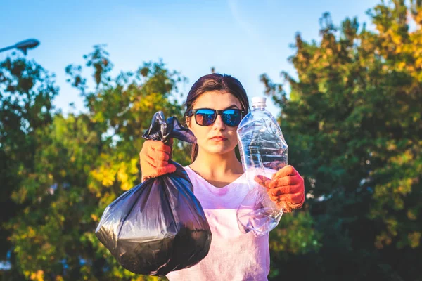 Молодая женщина держит полный мешок для мусора и использует пластиковую бутылку в руках. Концепция пластиковых и пищевых отходов. Чистая планета Земля, собирать мусор, избегать загрязнения, сохранить окружающую среду . — стоковое фото