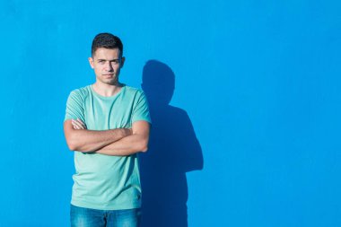 Mavi arka planda izole edilmiş kolları çapraz olan genç bir adam. Kopya alanı ile insanlar ve duygular kavramı.