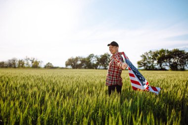 Genç vatansever çiftçi yeni hasatların arasında duruyor. Yeşil buğday tarlasında Amerikan bayrağıyla yürüyen çocuk ulusal bağımsızlık gününü kutluyor. 4 Temmuz konsepti