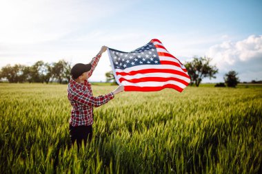 Genç vatansever çiftçi yeni hasatların arasında duruyor. Yeşil buğday tarlasında Amerikan bayrağıyla yürüyen çocuk ulusal bağımsızlık gününü kutluyor. 4 Temmuz konsepti
