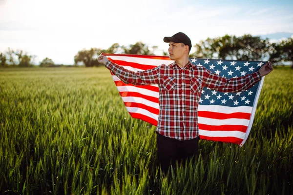 Genç vatansever çiftçi yeni hasatların arasında duruyor. Yeşil buğday tarlasında Amerikan bayrağıyla yürüyen çocuk ulusal bağımsızlık gününü kutluyor. 4 Temmuz konsepti
