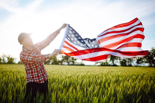 애국적 농부는 새로운 수확물 가운데서 국가의 기념일을 축하하는 밀밭에서 국기를 — 스톡 사진