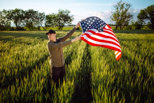 셔츠와 모자를 남자가 녹색밀 밭에서 바람에 나부끼는 국기를 펼치고 있습니다 — 스톡 사진