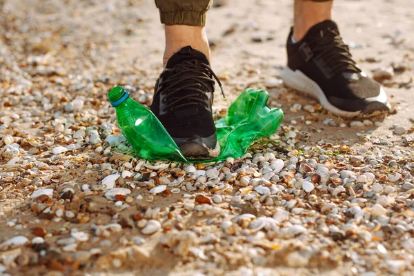 Young male volunteer picks up plastic garbage on the ocean coast. A man collects waste on the seaside to save ecology and protect environment. Recycle litter and pollution concept