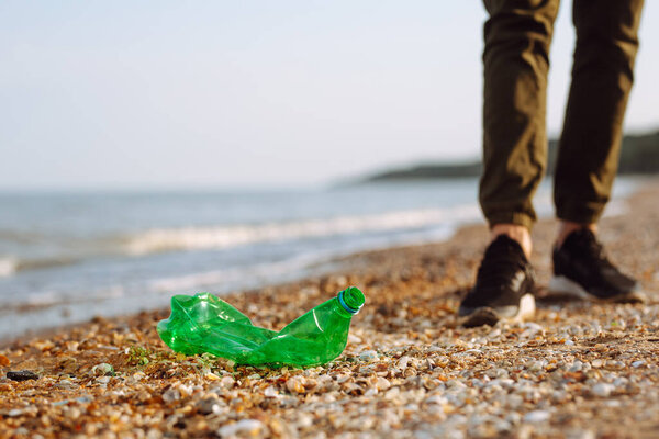 Young male volunteer picks up plastic garbage on the ocean coast. A man collects waste on the seaside to save ecology and protect environment. Recycle litter and pollution concept
