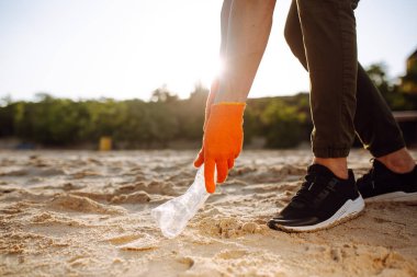 Genç gönüllü erkek, okyanus kıyısında plastik çöpleri topluyor. Bir adam ekolojiyi ve çevreyi korumak için deniz kıyısında atık topluyor. Çöp geri dönüşümü ve kirlilik kavramı