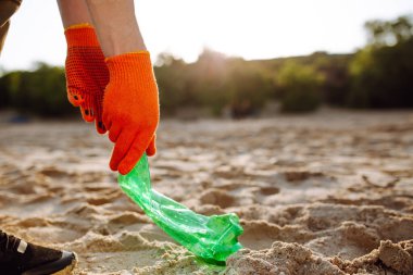 Genç gönüllü bir erkeğin elleri okyanus kıyısında plastik çöpleri topluyor. Bir adam ekolojiyi ve çevreyi korumak için deniz kıyısında atık topluyor. Çöp geri dönüşümü ve kirlilik kavramı