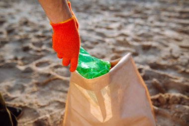 Genç gönüllü erkek, okyanus kıyısında plastik çöpleri topluyor. Bir adam ekolojiyi ve çevreyi korumak için deniz kıyısında atık topluyor. Çöp geri dönüşümü ve kirlilik kavramı