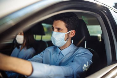 Genç taksi şoförü arabada steril tıbbi maske takıyor. Direksiyonun başındaki bir çocuk sosyal mesafeyi korumak için iş meseleleri için güvenli bir şekilde araba kullanıyor. Coronavirüs salgını konsepti