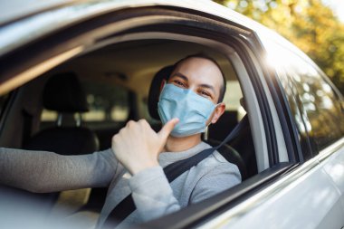 Genç adam, arabada steril maske takan bir tabela gibi baş parmağını kaldırdı. Taksi şoförü, yolcularını gideceği yere götürür. Sosyal mesafe, yeni normal, virüs yayılmış önleme ve tedavi kavramı