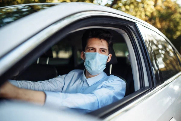 Genç adam steril tıbbi maske takarak direksiyon başında oturuyor. Erkek taksi şoförü Coronavirus salgını sırasında çok çalışıyor. Sosyal mesafe, virüs yayılımı önleme ve tedavi kavramı
