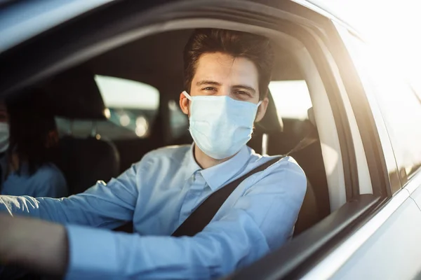 Young boy taxi driver gives passenger a ride wearing sterile medical mask. A man in the car behind the steering wheel works during coronavirus pandemic. Social distance and health safety concept