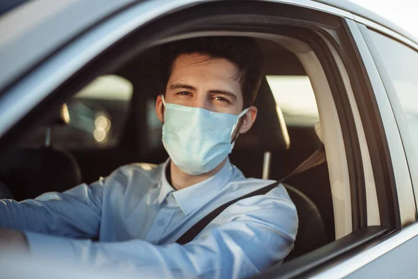 Young boy taxi driver gives passenger a ride wearing sterile medical mask. A man in the car behind the steering wheel works during coronavirus pandemic. Social distance and health safety concept