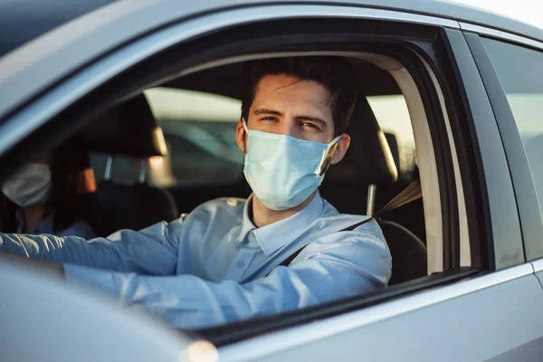 Young boy taxi driver gives passenger a ride wearing sterile medical mask. A man in the car behind the steering wheel works during coronavirus pandemic. Social distance and health safety concept