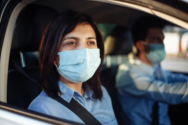 Young girl passenger takes a ride by taxi during the coronavirus pandemic quarantine. Woman looks out of the car window wearing sterile medical mask. Social distance and health safety concept