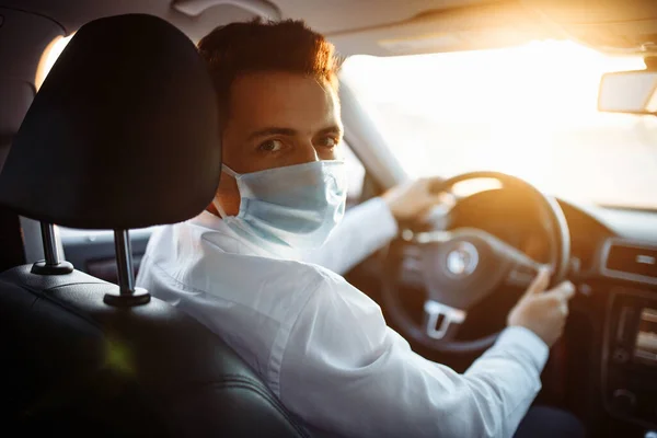 Genç taksi şoförü Coronavirus salgını sırasında steril tıbbi maske takıyor. Bir çocuk gün batımında trafikte bir araba sürer. Sosyal mesafe ve sağlık hizmeti kavramı