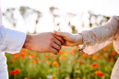 Kırmızı gelincik çiçek tarlasında el ele tutuşan sevgili çiftlerin yakınlaşması. Aşk ve birlikteliği gösteren romantik bir an. Aile değeri ve mutluluk kavramı