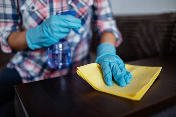 Cleaning dark table surface with spray detergent, blue rubber gloves and yellow dish cloth on work surface. Antibacterial work against coronavirus. Concept for hygiene, disinfection and health care