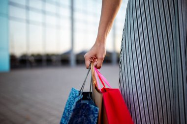 Yeni alınmış mal ve kıyafetlerle dolu bir kaç alışveriş çantası tutan çekici genç bir kadın. Kızın elinde bir sürü renkli paket dolusu bir şeyler var. Alışveriş ve harcama kavramı