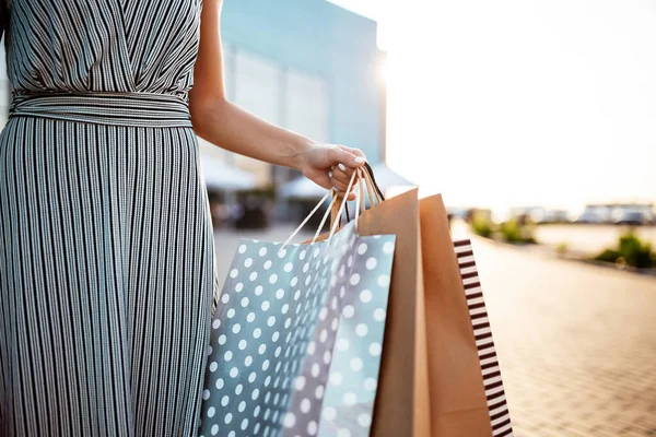 Closeup of young attractive woman holding a few shopping bags with newly purchased goods and clothes. Girl holds colourful packs full of bought things in her hands. Shopping and spendings concept