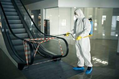 İşçi dezenfekte etmek boş bir alışveriş merkezinde yürüyen merdiveni dezenfekte eder. Böylece kalabalık alanlarda çovid-19 yayılmasını önler. Sağlık, temizlik, tecrit ve karantina kavramı