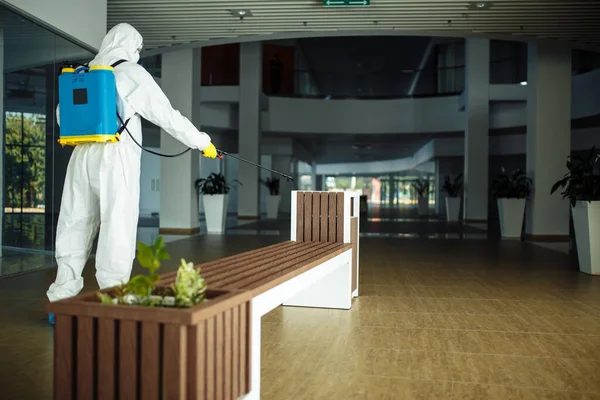 Hombre Con Traje Protector Está Desinfectando Banco Centro Comercial Vacío —  Fotos de Stock