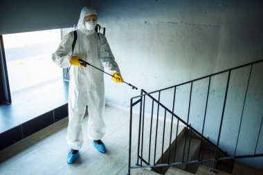 Alışveriş merkezindeki merdivenleri antiseptikle temizleyen işçi kovid 19 yayılmasını önlemek için. Dezenfekte kıyafeti giymiş bir adam merdivenleri spreyliyor. Sağlık, karantina ve hijyen kavramı