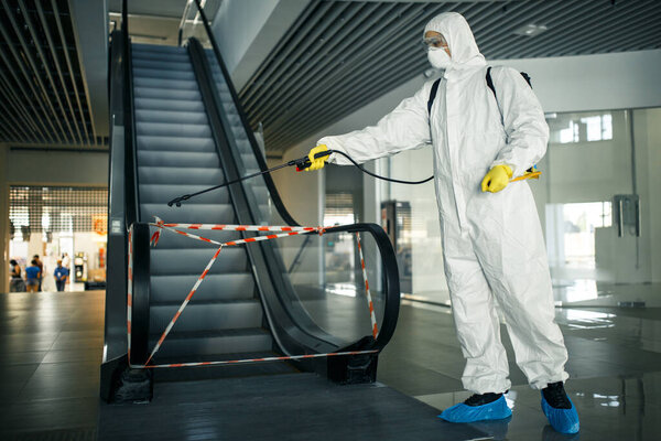 Дезинфицирующий работник дезинфицирует эскалатор спреем в пустом торговом центре, чтобы предотвратить распространение ковид-19 в общественных местах. Здравоохранение, чистота, изоляция и карантин