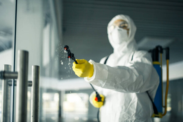 A man wearing disinfection suit spraying with sanitizer the glass doors' handles in an empty shopping mall to prevent covid-19 spread. Health awareness, clean, defence concept