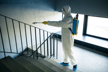 Alışveriş merkezindeki merdivenleri antiseptikle temizleyen işçi kovid 19 yayılmasını önlemek için. Dezenfekte kıyafeti giymiş bir adam merdivenleri spreyliyor. Sağlık, karantina ve hijyen kavramı