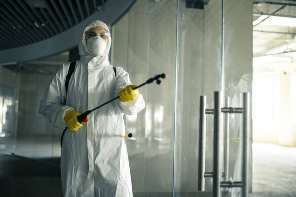 Sanitary worker sprays an empty business center with antiseptical liquid to prevent covid-19 spread. A man wearing disinfection suit cleaning up the shopping mall. Nobody, health, isolated concept