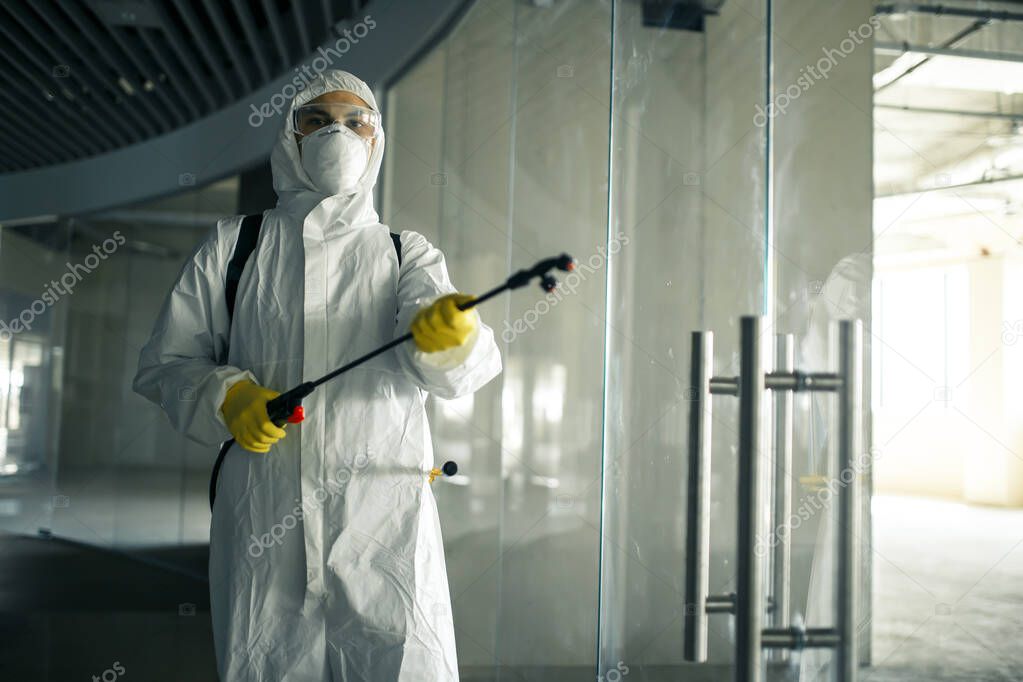 Sanitary worker sprays an empty business center with antiseptical liquid to prevent covid-19 spread. A man wearing disinfection suit cleaning up the shopping mall. Nobody, health, isolated concept