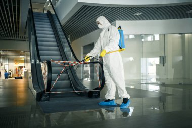 İşçi dezenfekte etmek boş bir alışveriş merkezinde yürüyen merdiveni dezenfekte eder. Böylece kalabalık alanlarda çovid-19 yayılmasını önler. Sağlık, temizlik, tecrit ve karantina kavramı