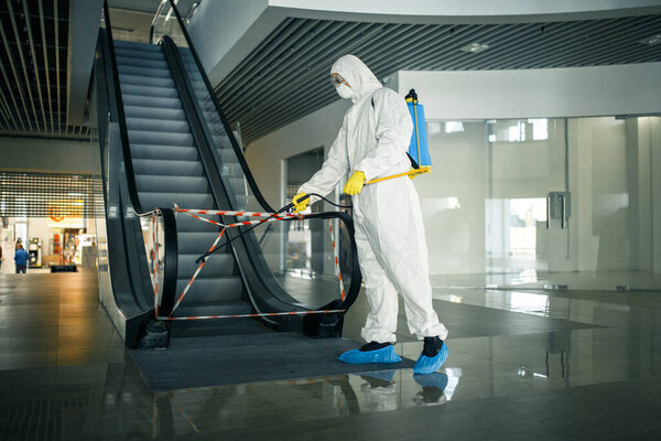 Sanitizing worker disinfects the escalator with a spray at the empty shopping mall to prevent the covid-19 spread in public places. Healthcare, clean, isolation and quarantine concept