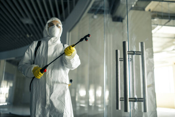 Sanitary worker sprays an empty business center with antiseptical liquid to prevent covid-19 spread. A man wearing disinfection suit cleaning up the shopping mall. Nobody, health, isolated concept
