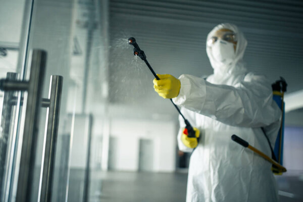 Sanitary worker sprays an empty business center with antiseptical liquid to prevent covid-19 spread. A man wearing disinfection suit cleaning up the shopping mall. Nobody, health, isolated concept