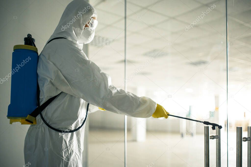 Sanitary worker sprays an empty business center with antiseptical liquid to prevent covid-19 spread. A man wearing disinfection suit cleaning up the shopping mall. Nobody, health, isolated concept