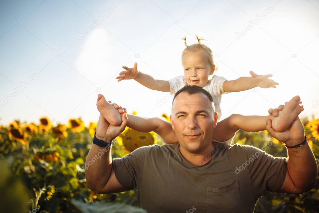 Father and daughter in sunflower field with their hands raised enjoy the summer season together. A man and his little child having fun among the sunflowers. Family values, freedom, love concept