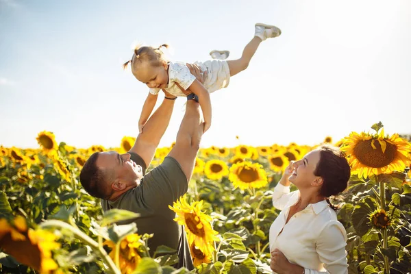 Happy family having fun in the field of sunflowers. Father and mother throw their daughter in the air and smile. Girl likes playing with her parents. Summer season, freedom, family value concept